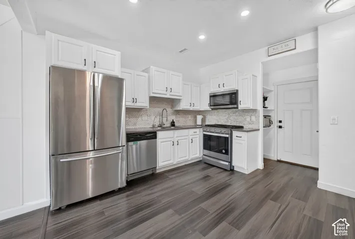Kitchen featuring white shaker-style cabinetry, stainless steel appliances, patterned tile backsplash, solid-surface countertops, and wood-finish flooring