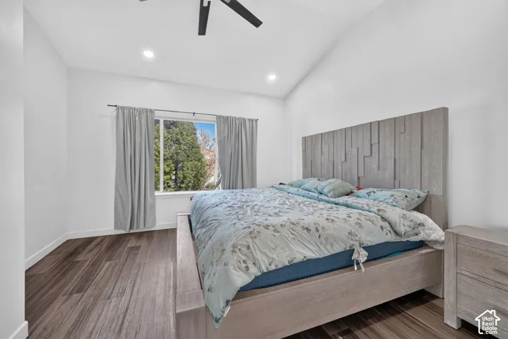 Vaulted ceiling featuring a recessed lighting array and a matte black ceiling fan, paired with wood-finish flooring and a window with exterior foliage