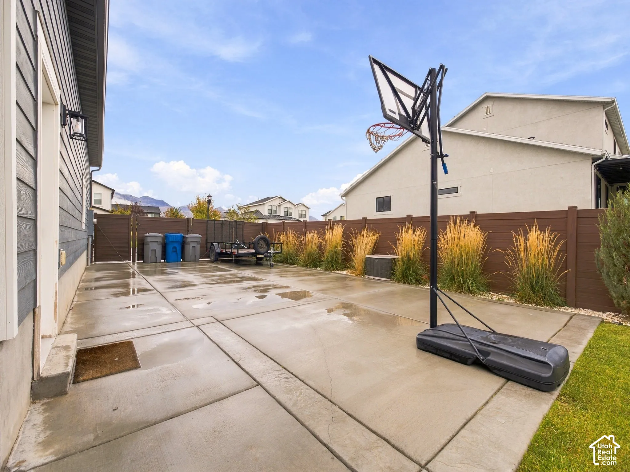Spacious concrete side yard enclosed by a horizontal privacy fence featuring tall ornamental grasses