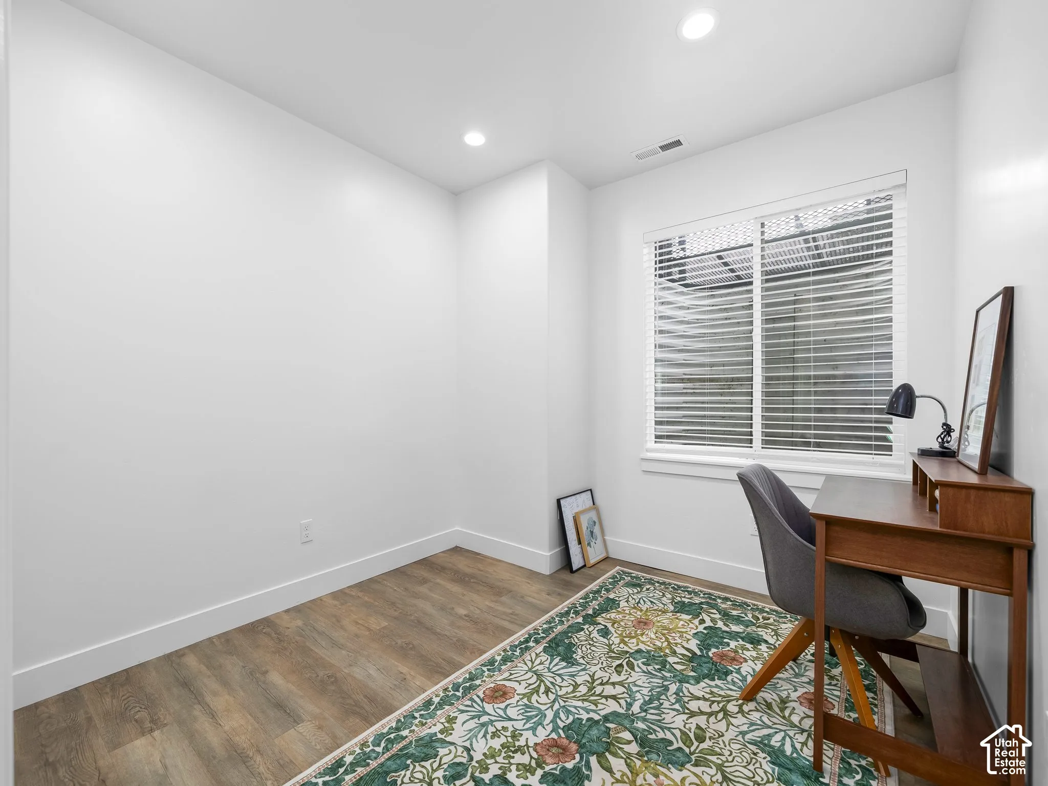 Interior room featuring wood-finish flooring, white walls, recessed ceiling lighting, and a window with horizontal blinds
