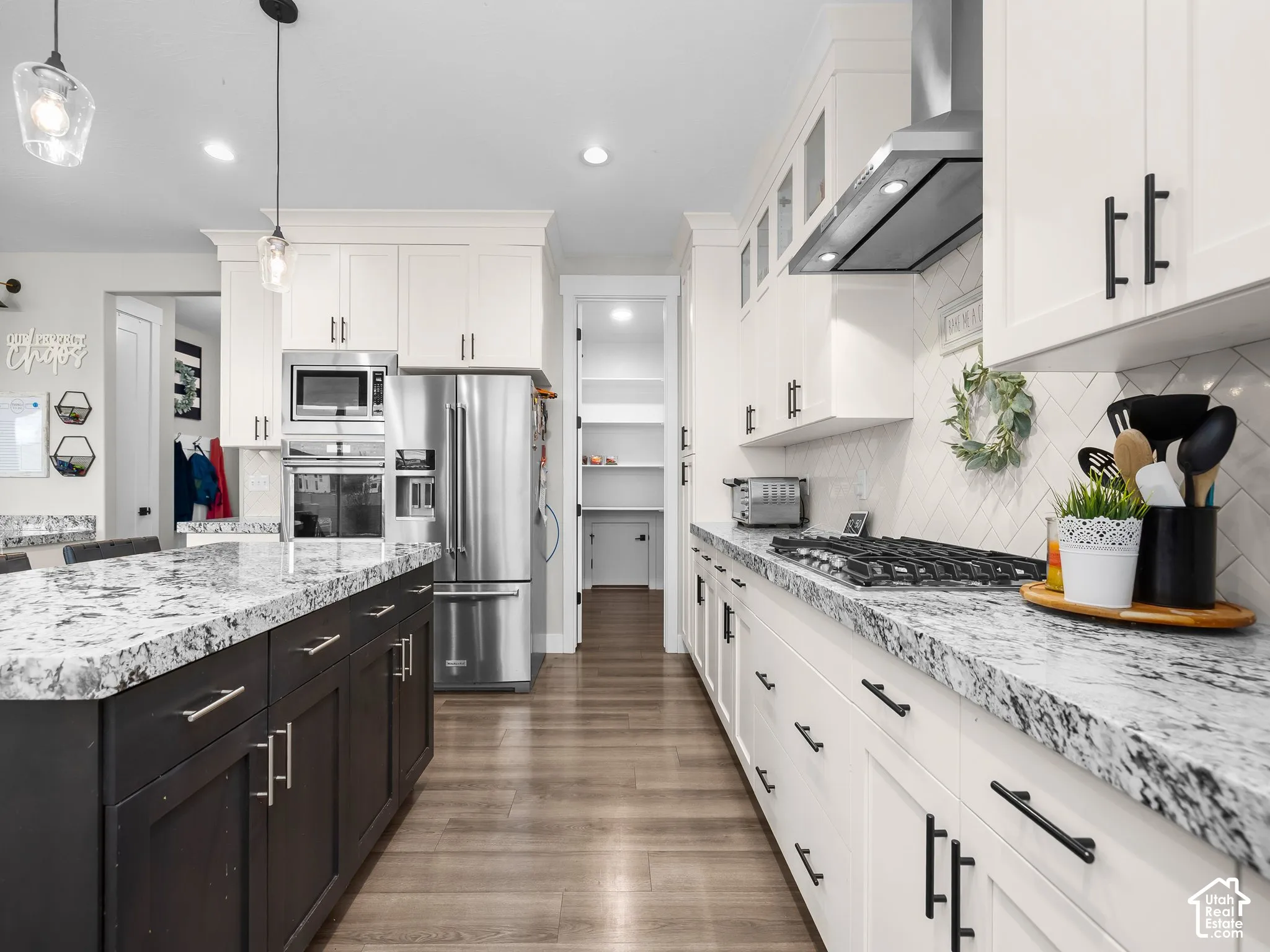 Kitchen featuring a dark-toned central island, white cabinetry with matte black hardware, stone-finish countertops, herringbone-pattern backsplash, and stainless steel built-in appliances