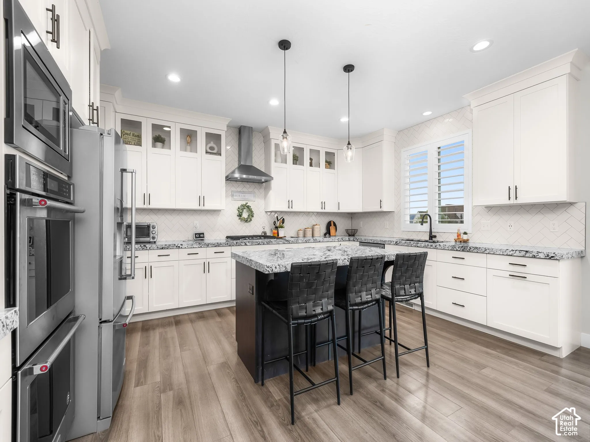 Kitchen featuring white shaker-style cabinetry, a central island with a contrasting base, stone-surface countertops, wood-finish flooring, and stainless steel built-in double ovens