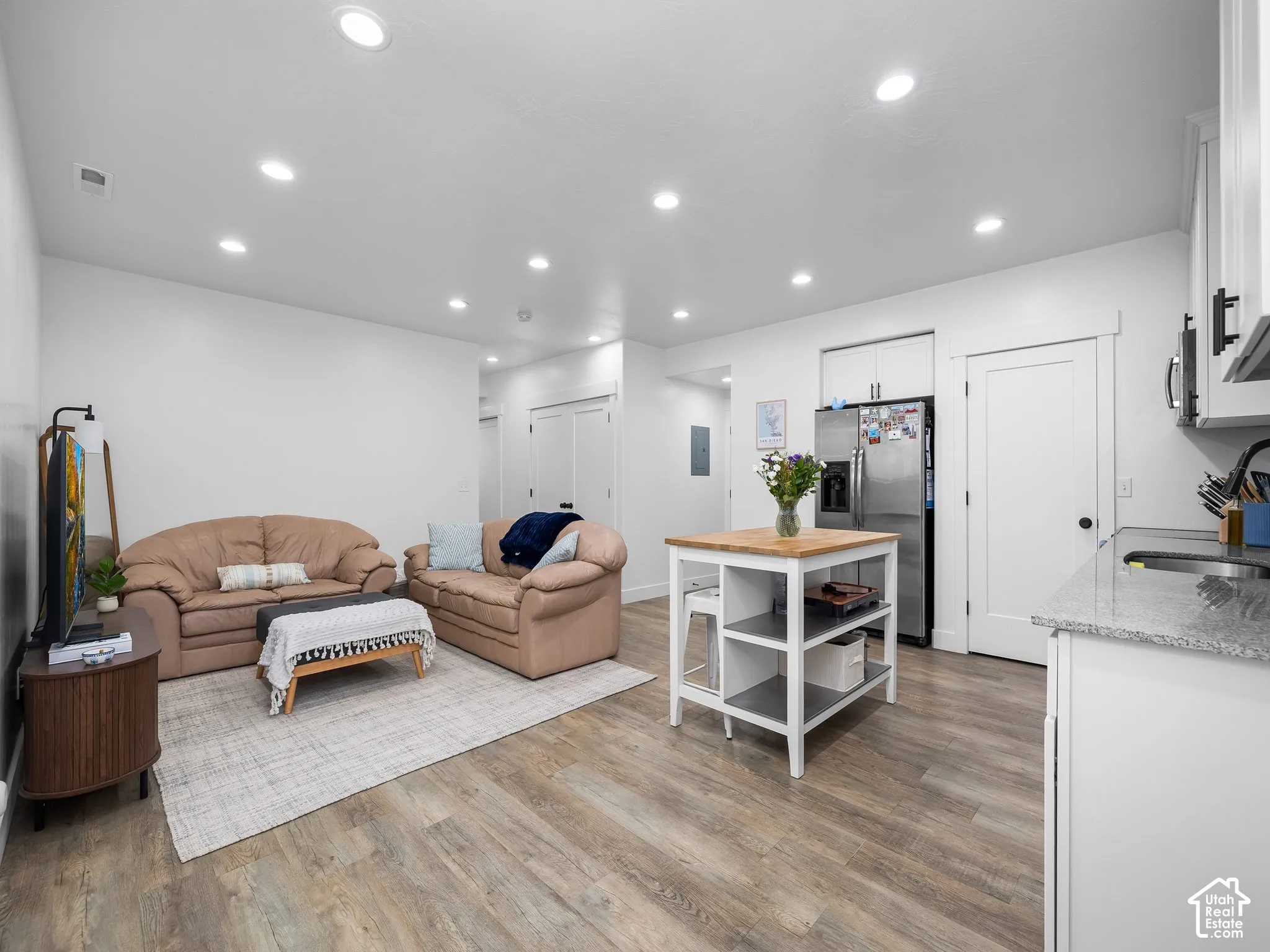 Open-concept area featuring wood-finish flooring, recessed lighting, stone countertops, and crisp white cabinetry
