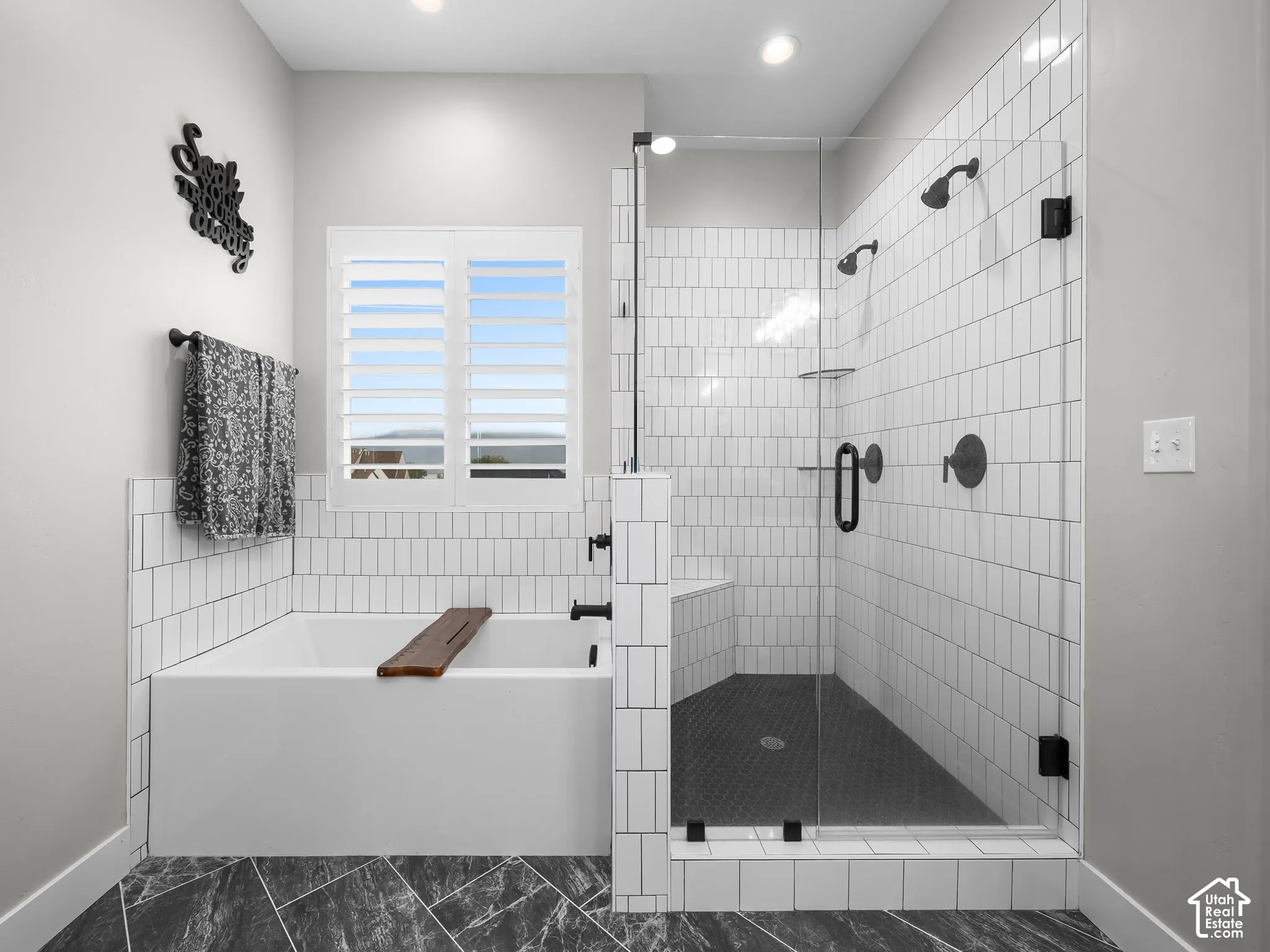 Bathroom featuring a soaking tub, glass-enclosed shower with dual shower heads, white subway tile surround, and patterned stone-finish flooring