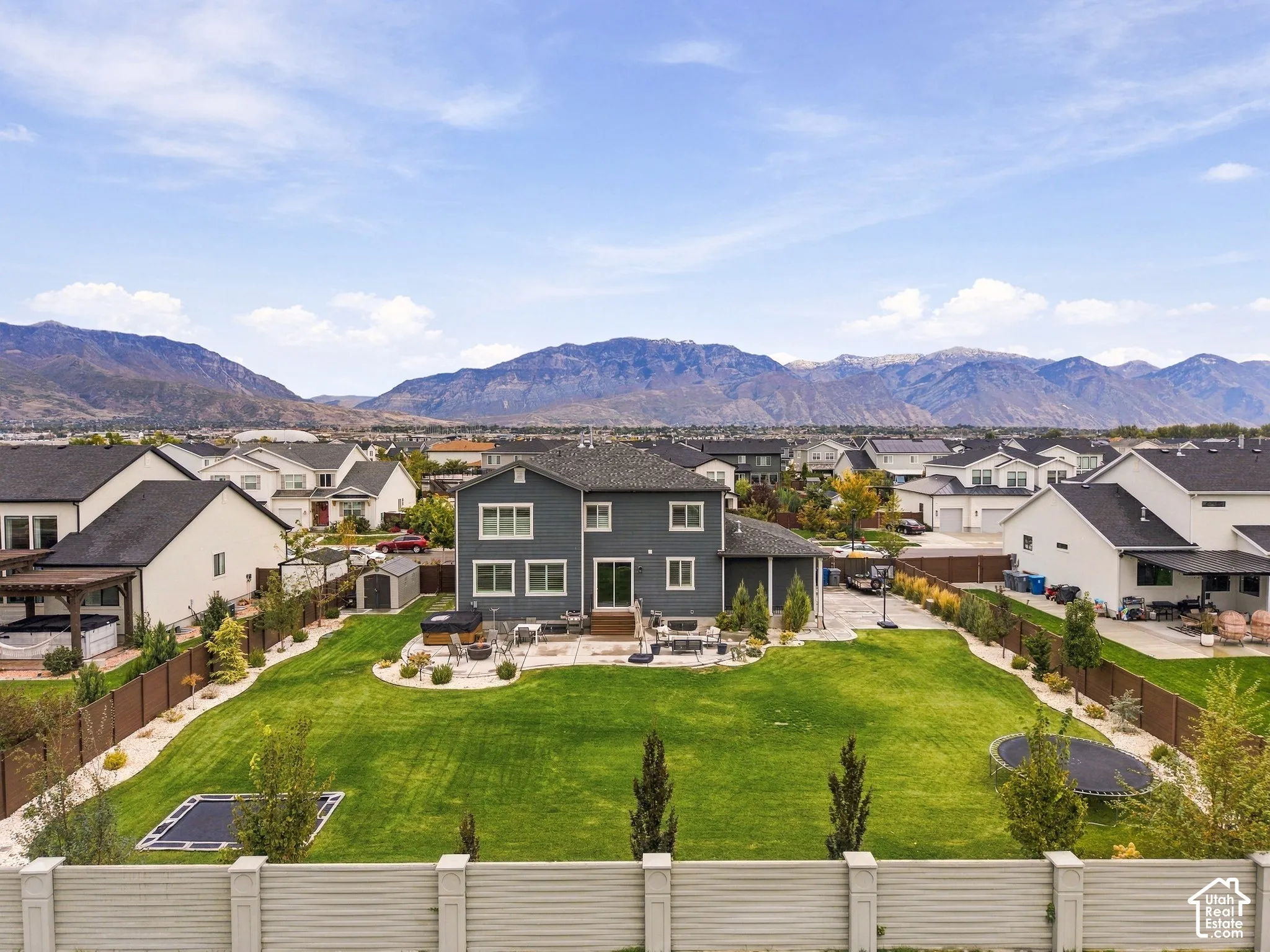 Two-story residence featuring horizontal lap siding, a rear concrete patio, an expansive lawn, mountain backdrop, and a perimeter privacy fence