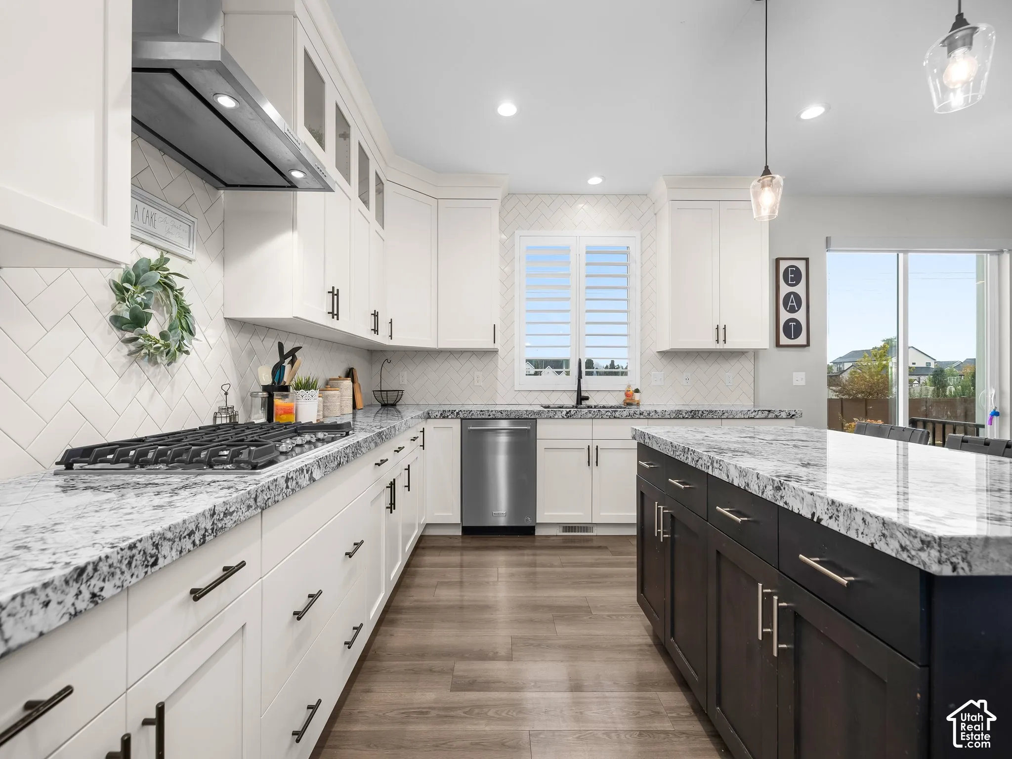 Kitchen featuring white shaker-style cabinetry, dark wood-finish kitchen island, stone-patterned countertops, herringbone-patterned tile backsplash, and stainless steel appliances