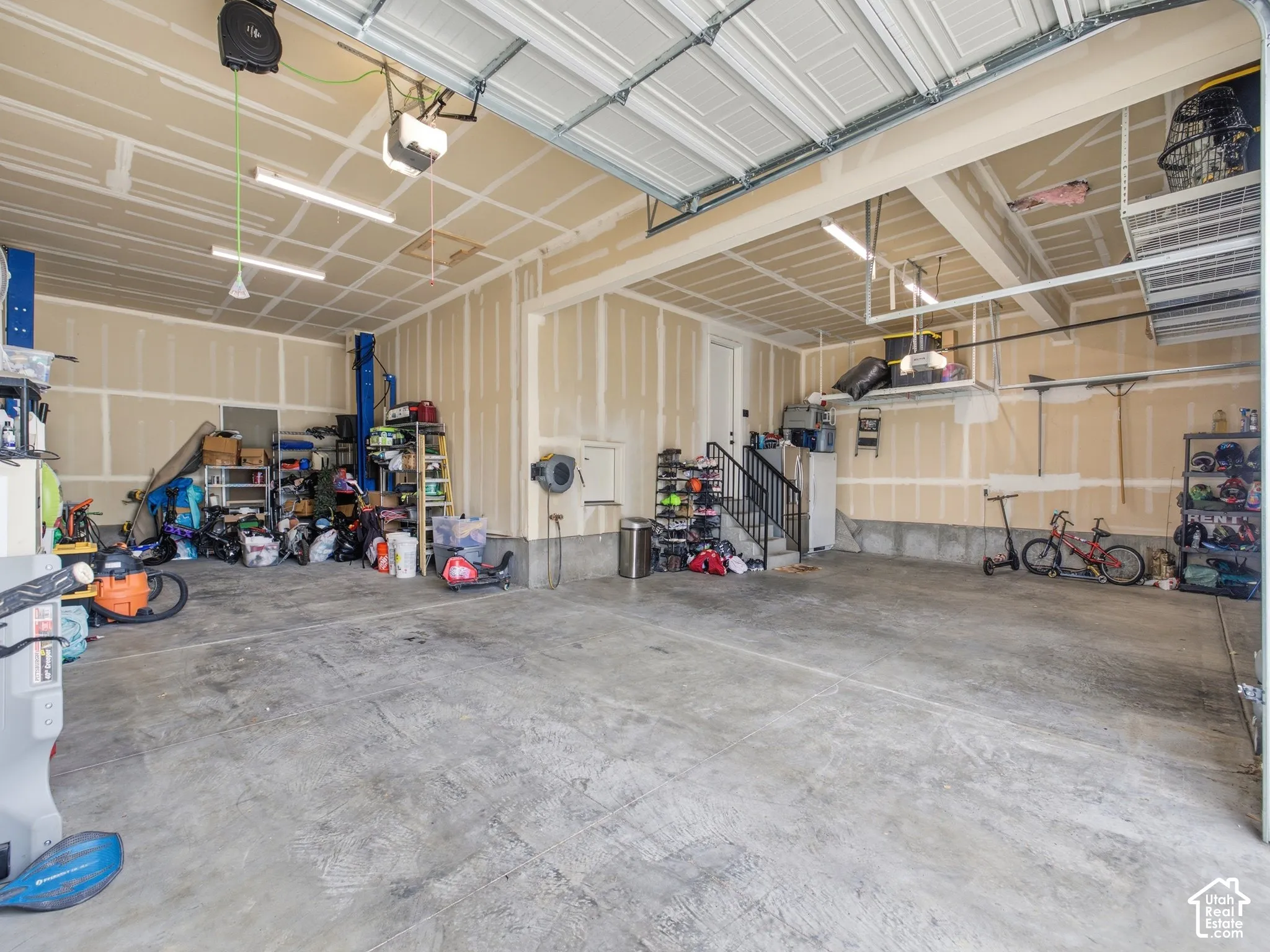 Multi-car garage featuring a concrete floor, built-in metal overhead storage racks, integrated lighting, and a secondary staircase