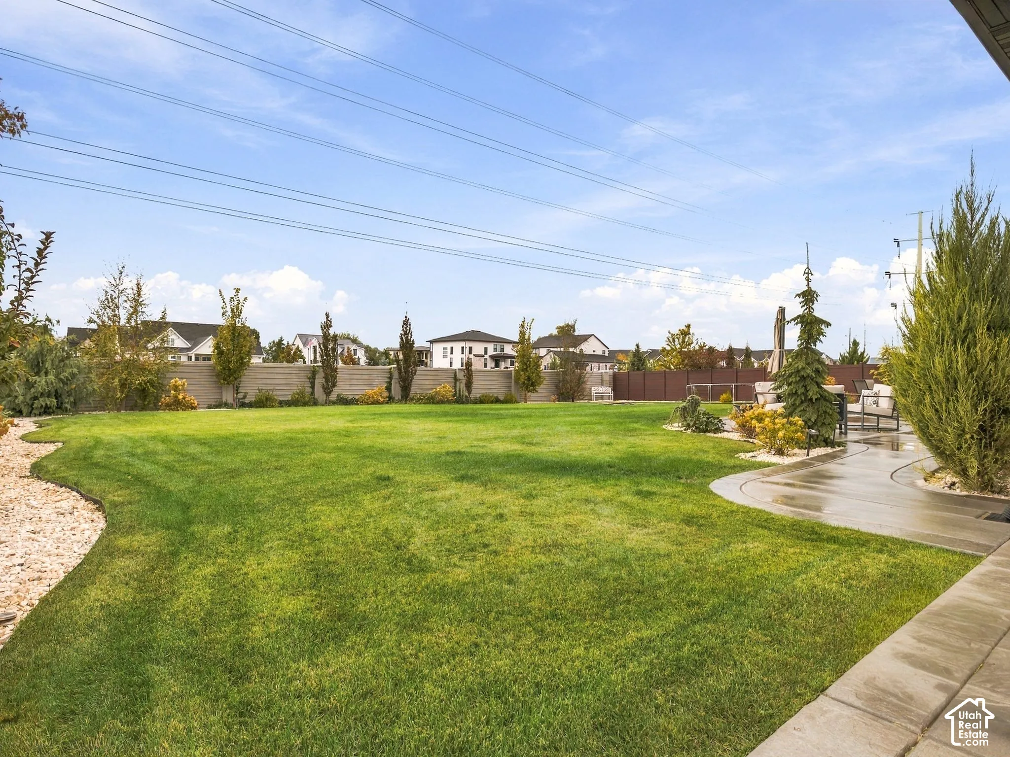 Expansive backyard featuring a manicured lawn, concrete patio, perimeter privacy fencing, decorative rock beds, and mature landscaping