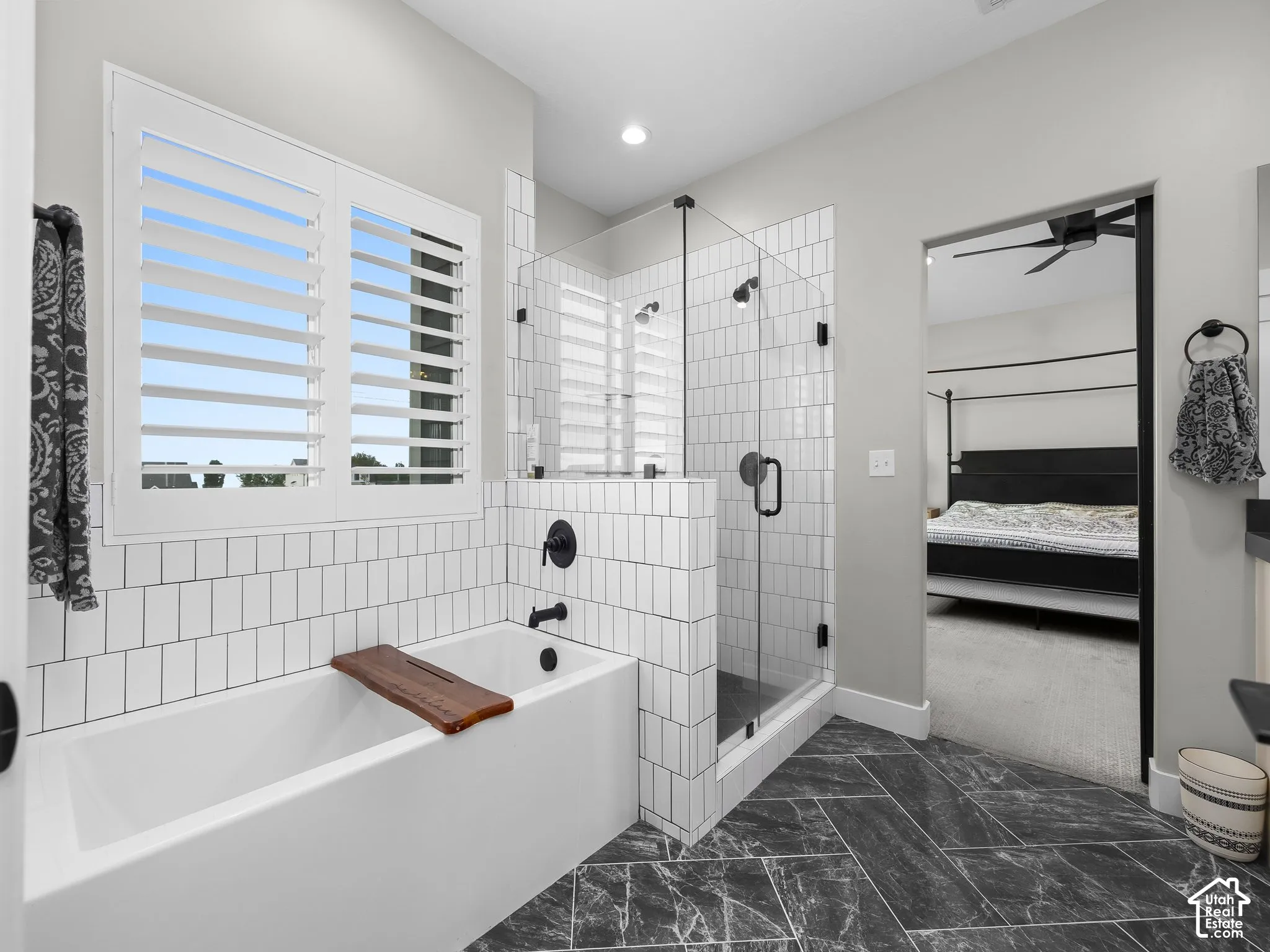 Bathroom featuring a deep soaking tub, glass-enclosed shower with white subway-style tile, matte black fixtures, and stone-finish floor tile in a herringbone pattern