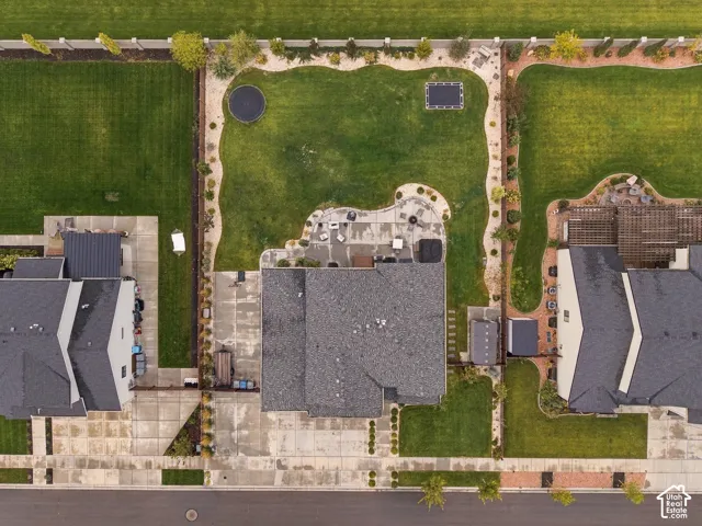 Aerial perspective of the property featuring a concrete patio, expansive lawn, stone-bordered landscaping beds, and a concrete driveway