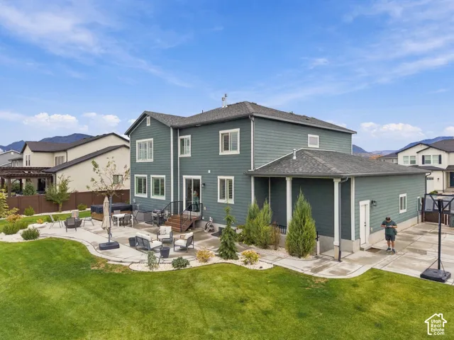 Two-story exterior with horizontal siding, covered side patio, expansive concrete hardscaping, manicured lawn, and mountain backdrop