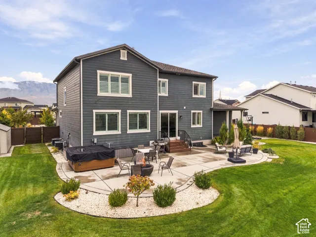 Two-story exterior with horizontal siding, expansive concrete patio, built-in hot tub, landscaping with gravel mulch, and mountain scenery