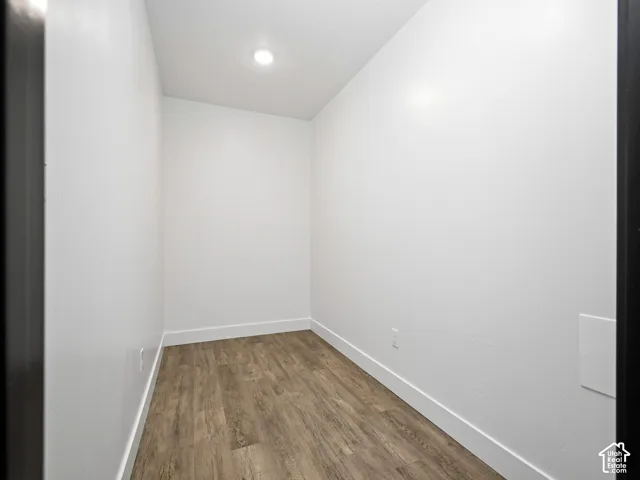 Neutral-toned interior space featuring wood-finish flooring, smooth white walls, and a recessed ceiling light fixture