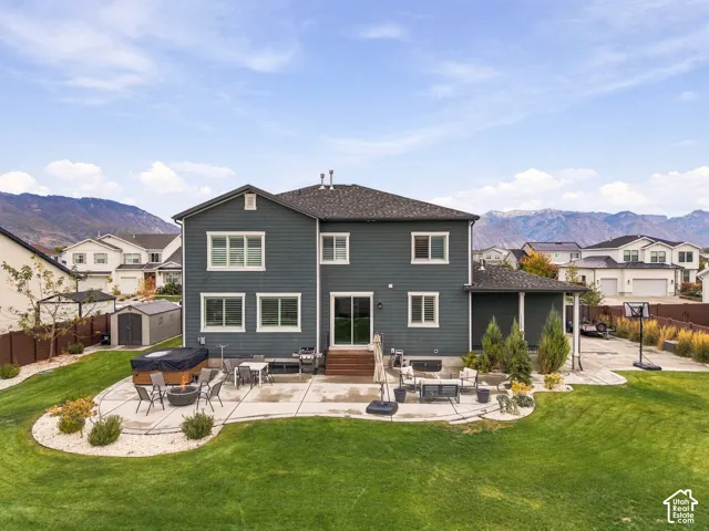 Two-story residence with horizontal siding, expansive concrete patio, built-in hot tub, manicured lawn, and mountain backdrop