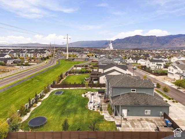 Aerial perspective of a multi-story residence featuring a large manicured lawn, stone-paver patio, privacy fencing, and mountain backdrop