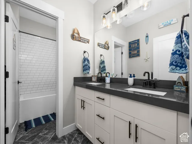 Bathroom featuring a dual-sink vanity with matte black fixtures, quartz countertop, large vanity mirror, four-light glass pendant fixture, and shower-tub combination with white subway tile surround