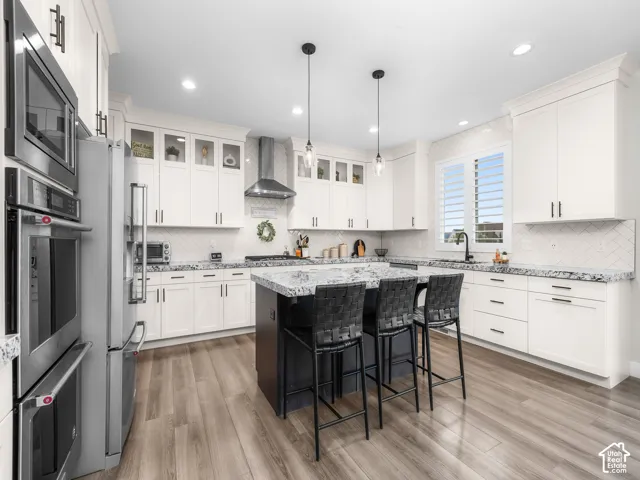Kitchen featuring white shaker-style cabinetry, a central island with a contrasting base, stone-surface countertops, wood-finish flooring, and stainless steel built-in double ovens
