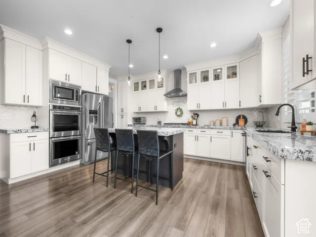 Kitchen featuring white cabinetry, stone countertops, stainless steel double wall ovens, wood-finish flooring, and a central kitchen island