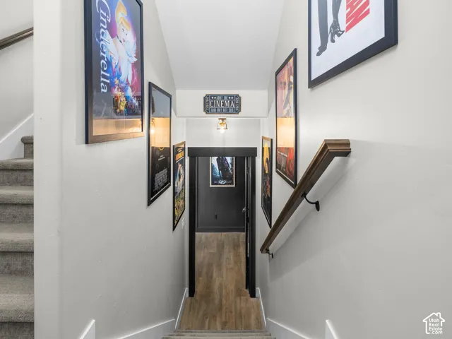 Staircase featuring neutral-toned carpeting, a stained wood handrail with matte black hardware, and wood-finish flooring