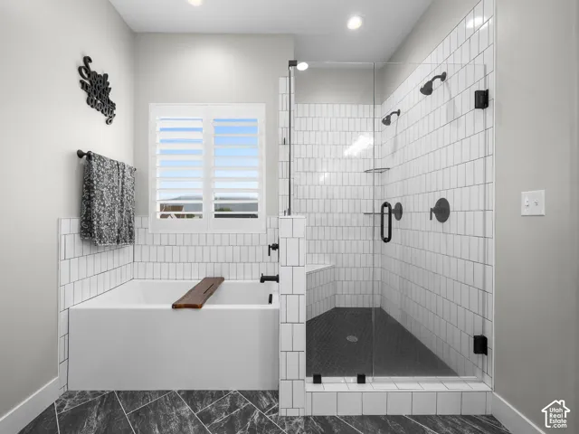 Bathroom featuring a soaking tub, glass-enclosed shower with dual shower heads, white subway tile surround, and patterned stone-finish flooring