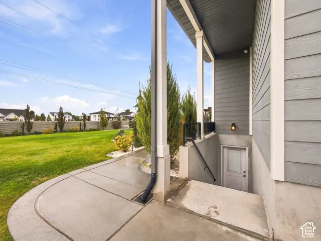 Covered concrete patio with siding exterior, subterranean staircase entrance, metal handrails, and exterior wall-mounted lighting