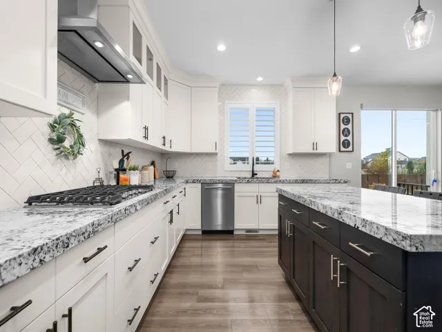 Kitchen featuring white shaker-style cabinetry, dark wood-finish kitchen island, stone-patterned countertops, herringbone-patterned tile backsplash, and stainless steel appliances