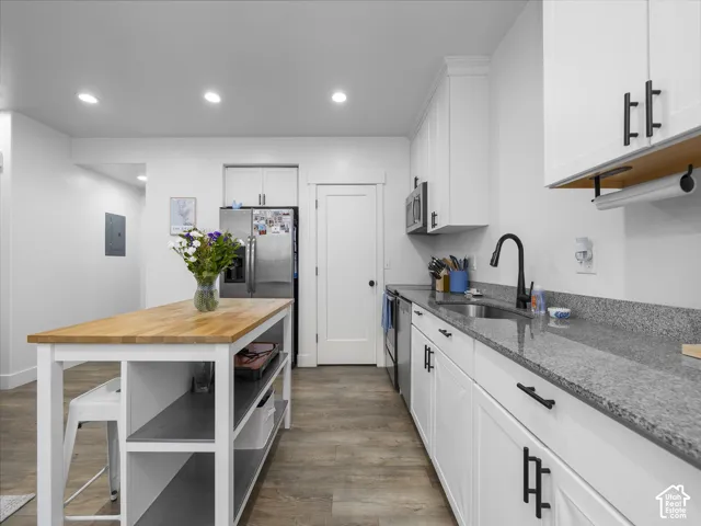 Kitchen featuring white shaker-style cabinetry, stone-surface countertops, wood-top island with open shelving, matte black hardware, and recessed lighting