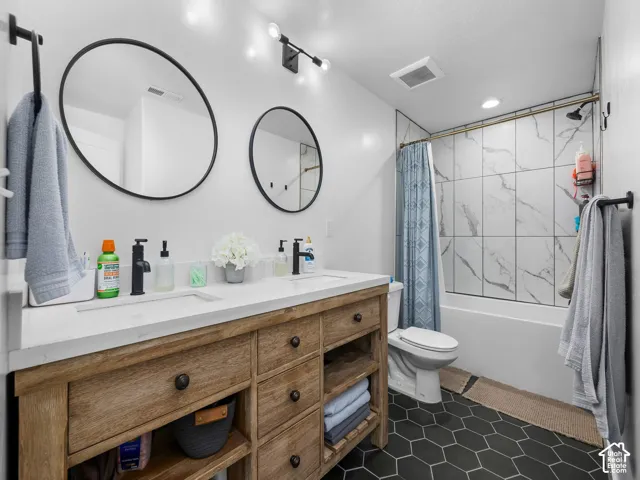 Double vanity featuring a light wood-finish cabinet with integrated shelving, quartz countertop, matte black fixtures, and round mirrors with black frames, complemented by geometric black floor tile and full-height tiled shower surround