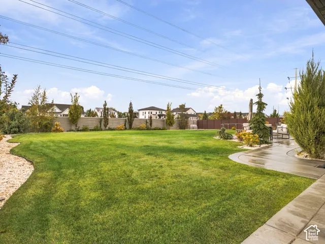 Expansive backyard featuring a manicured lawn, concrete patio, perimeter privacy fencing, decorative rock beds, and mature landscaping