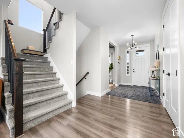 Entryway featuring wood-finish flooring, a staircase with metal balusters and a wood handrail, a paneled front door with a transom window, and a multi-arm modern pendant light fixture