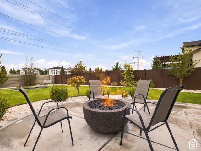 Backyard featuring a concrete patio, stone fire pit, fenced perimeter, and landscaped lawn
