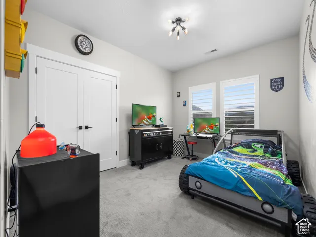 Neutral interior room featuring neutral carpeting, double-door closet with matte black hardware, and dual windows equipped with plantation shutters