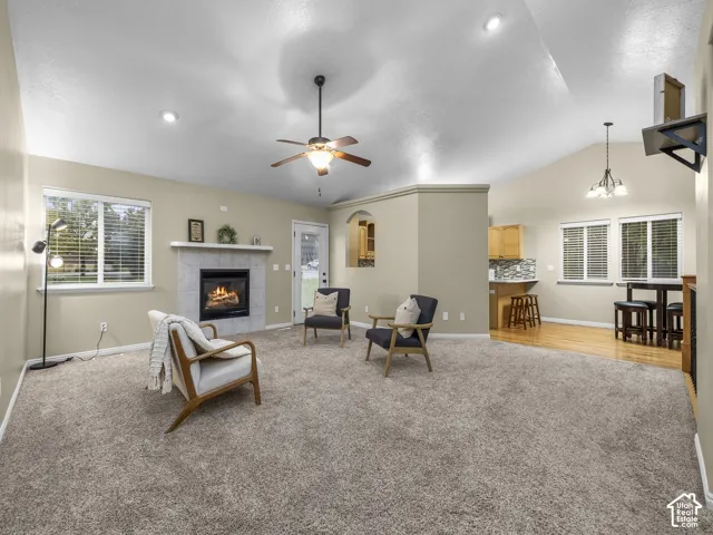 Vaulted ceilings, tiled fireplace surround, recessed lighting, ceiling fan, and wood-finish flooring