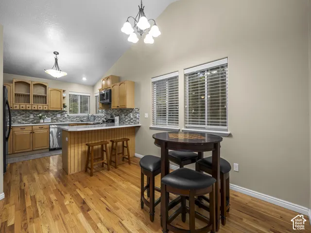 Kitchen featuring vaulted ceilings, wood-finish flooring, light wood cabinetry, a breakfast bar, and patterned tile backsplash