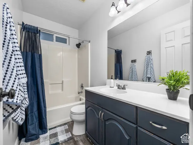 Bathroom featuring a dark-toned vanity cabinet with a light-colored countertop, integrated sink, full-width mirror, and a combination tub and shower enclosure with a surround