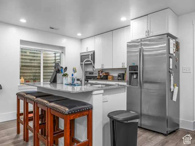 Kitchen featuring white shaker-style cabinetry, stone-finish countertops, stainless steel appliances, and wood-finish flooring