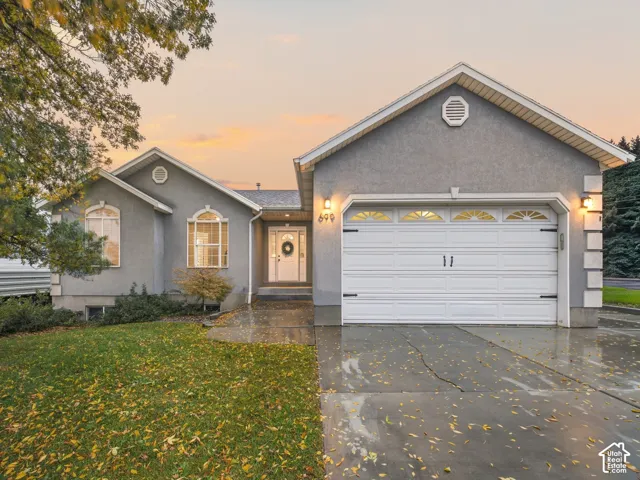 Stucco exterior residence featuring a gabled roofline, an attached two-car garage, stone-accented corners, and arched window detailing