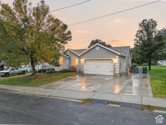 Single-story exterior featuring a light-toned stucco facade, dual-gabled roofline, two-car garage, and a wide concrete driveway