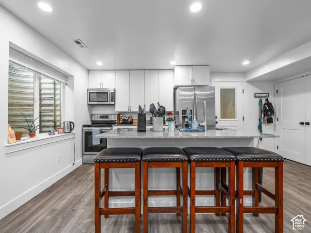 Kitchen featuring white flat-panel cabinetry, stone-finish countertops, stainless steel appliances, recessed lighting, and wood-finish flooring