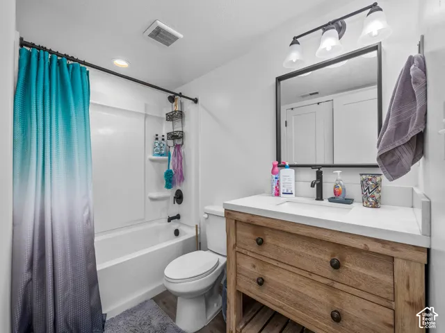 Bathroom featuring a wood-finish vanity with a stone countertop, an integrated rectangular sink, a black metal framed mirror, three-light vanity fixture, and a tub-shower combination with matte black hardware