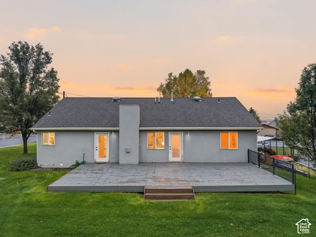Single-story residence featuring a large rear deck, two glass-paneled exterior doors, a central chimney, and mature trees on a lawn
