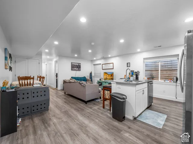 Open concept interior featuring recessed lighting, wood-finish flooring, and a kitchen island with a stainless steel undermount sink and faucet