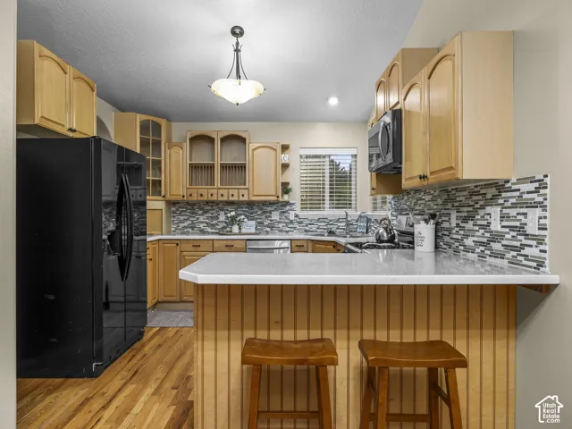 Kitchen featuring light-finish cabinetry, stone-composite countertops, multi-tonal glass tile backsplash, wood-finish flooring, and a peninsula with beadboard detailing