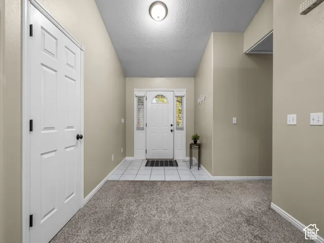 Entryway featuring a vaulted ceiling, neutral wall color, tiled floor landing, carpeted flooring, and a glass-paneled entry door with sidelights