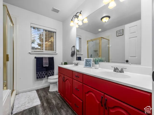 Dual-sink vanity with a solid-surface countertop, wood-finish flooring, full-width wall mirror, and a glass-enclosed shower