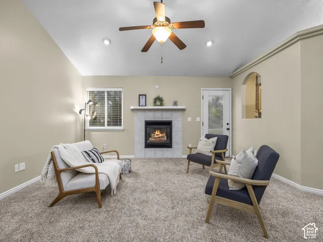 Vaulted ceilings, neutral wall tones, carpeted flooring, a fireplace featuring a tile surround and mantel, and an arched wall niche