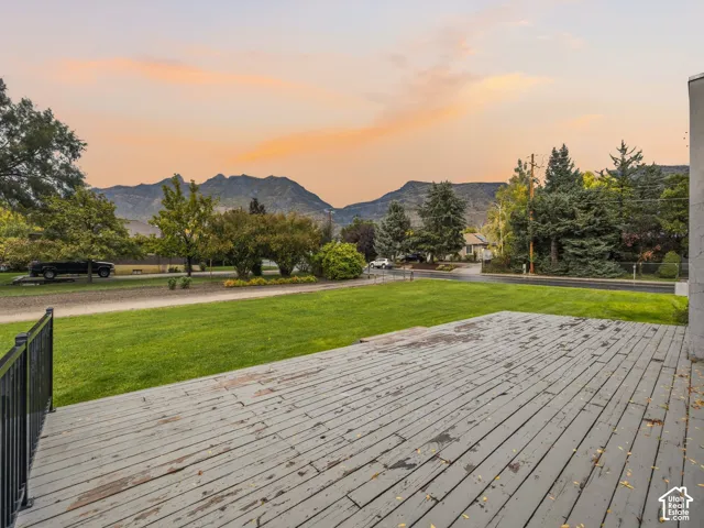 Elevated wood-plank deck featuring a metal railing, expansive lawn, and mountain backdrop
