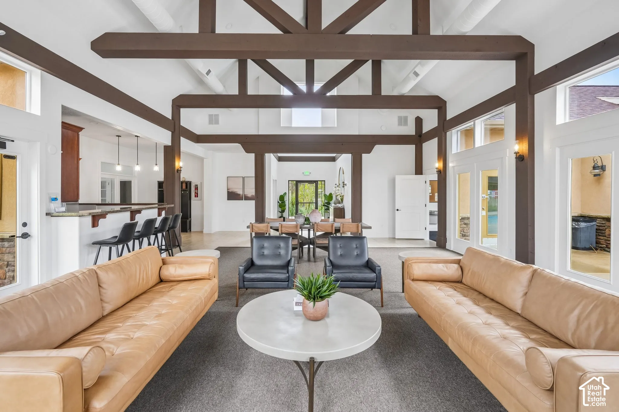Vaulted ceilings with exposed timber trusses, neutral wall palette, extensive natural light, stone-finish breakfast bar, and multiple glass-pane exterior doors