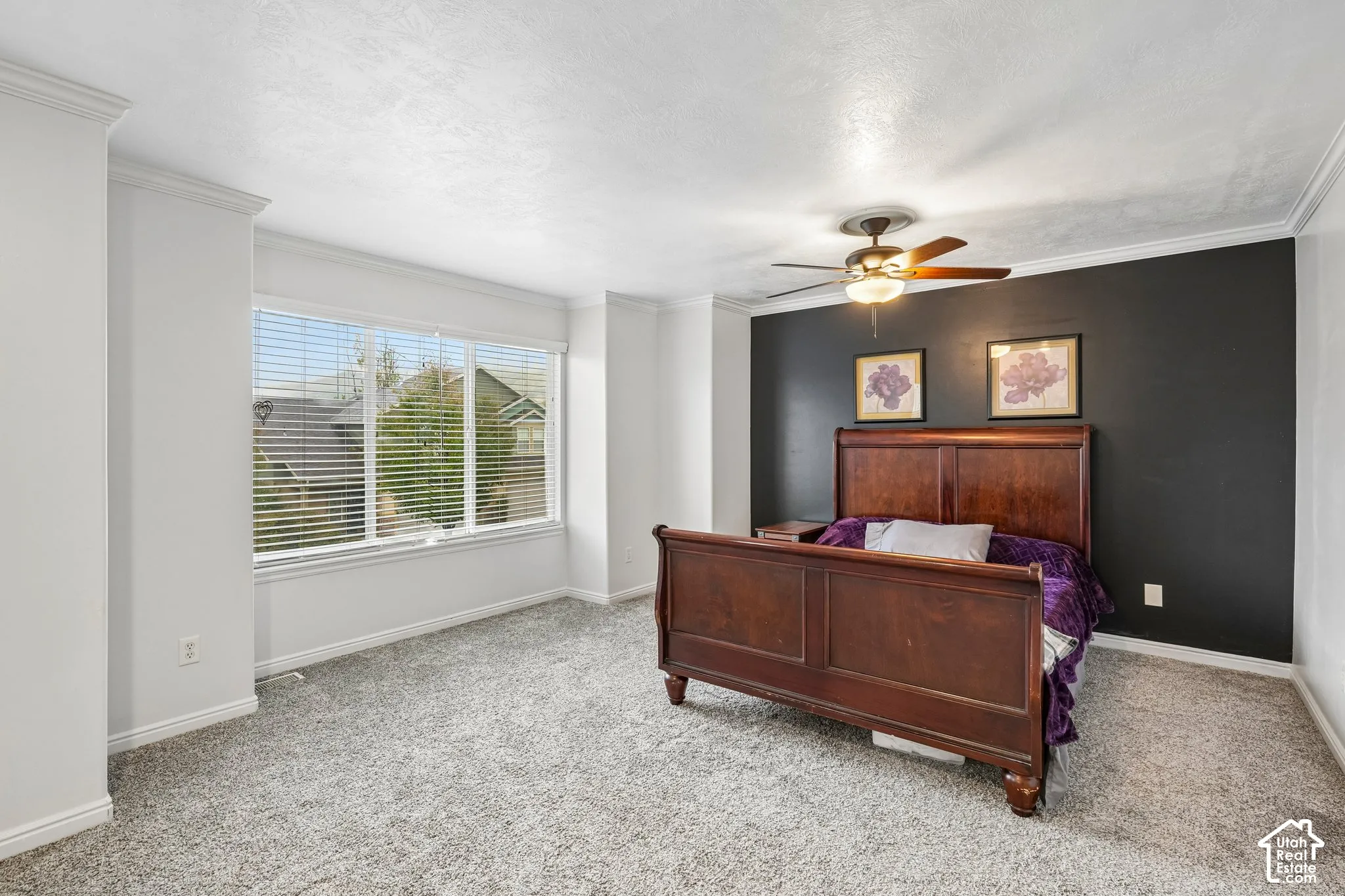 Room featuring neutral carpeting, a dark accent wall, crown molding, a multi-pane window with blinds, and a central ceiling fan with integrated lighting