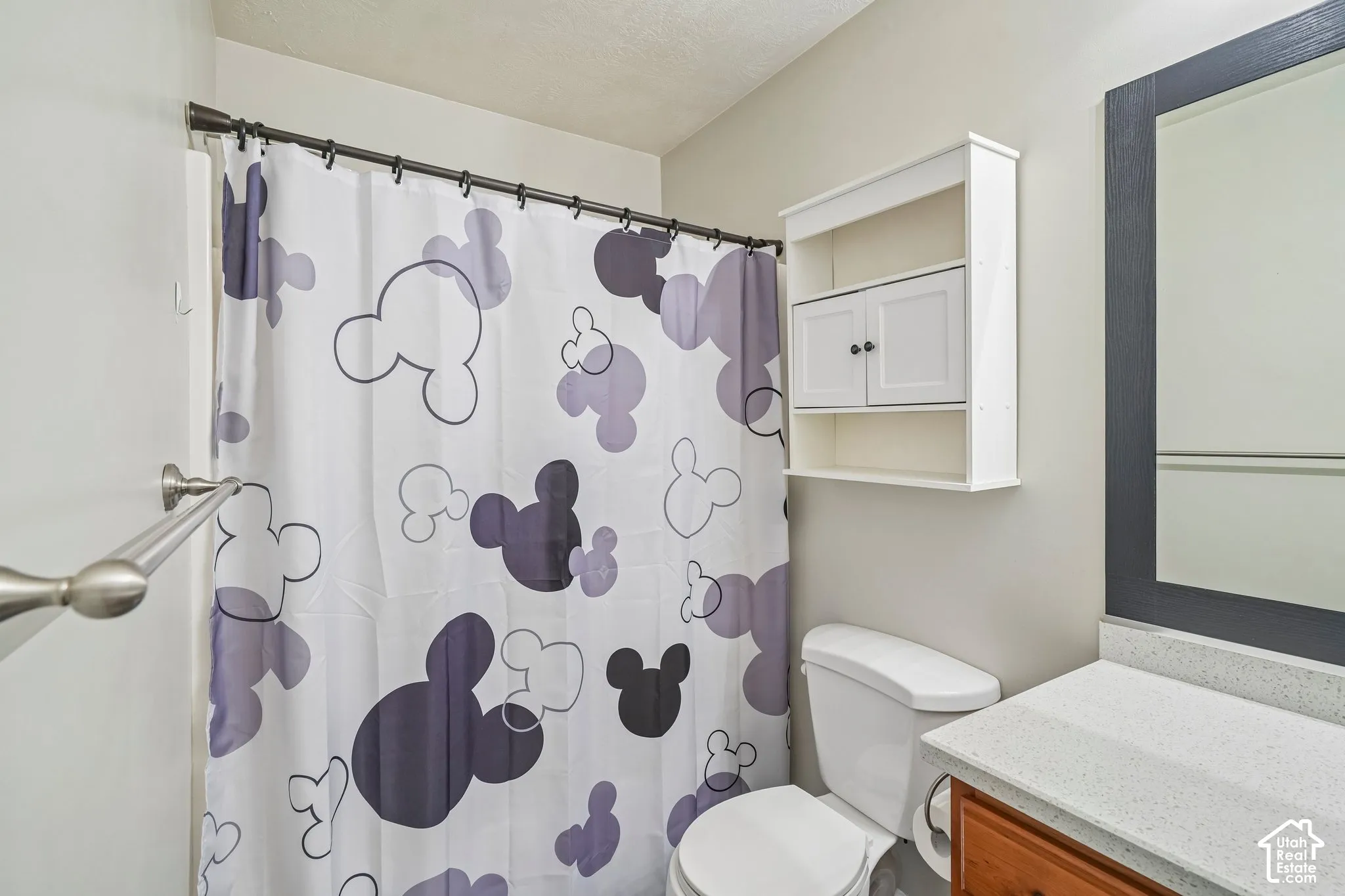 Bathroom featuring a vanity with a light-toned solid surface countertop, a dark-framed wall mirror, wall-mounted white cabinetry, and a brushed nickel towel bar